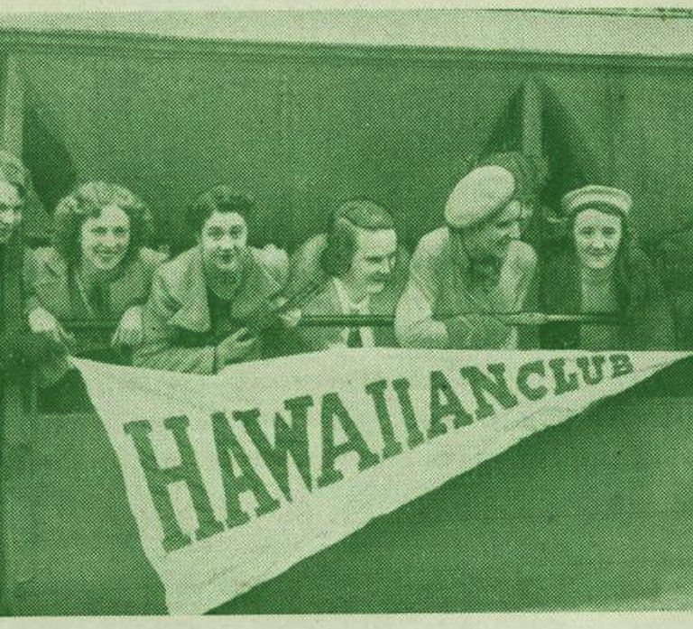 A grainy photo of a group of 8 women leaning over a balcony holding a penant that says Hawaiian Club. From The Hawaiian Times magazine, 1939.