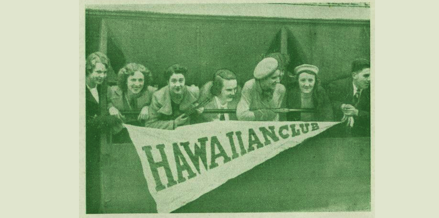 A grainy photo of a group of 8 women leaning over a balcony holding a penant that says Hawaiian Club. From The Hawaiian Times magazine, 1939.